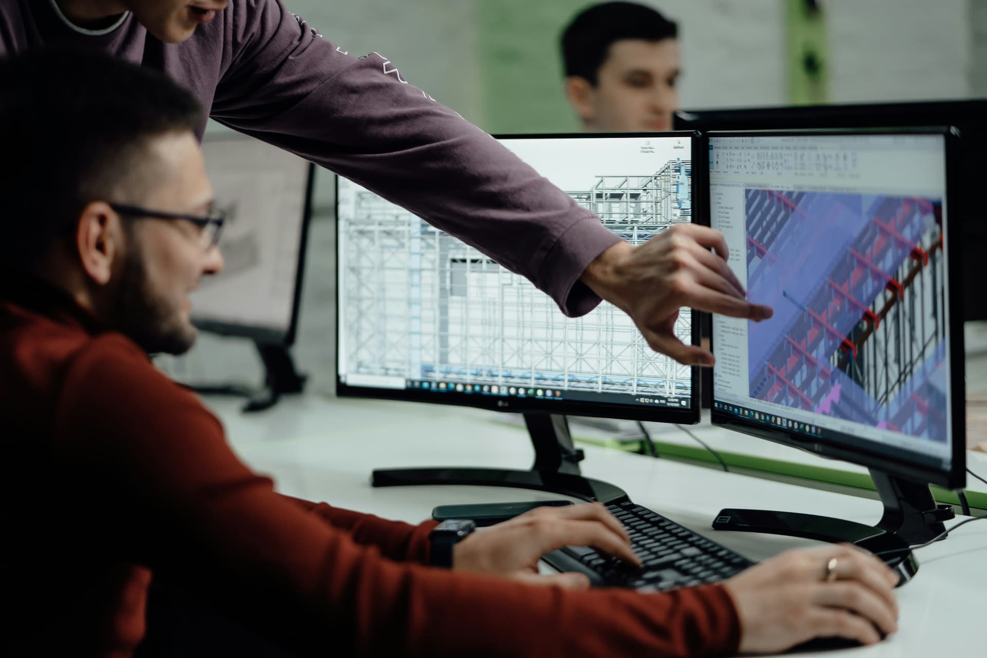 Two professionals collaborating on BIM software with dual monitors displaying 3D building models and architectural drawings